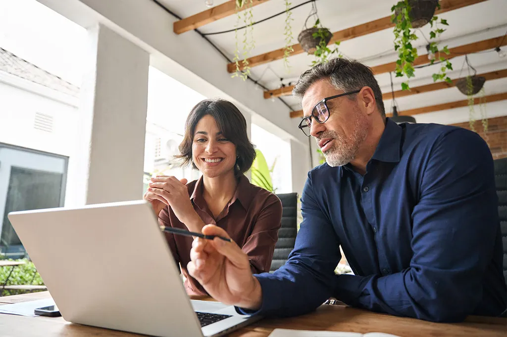 Real estate agent with client looking on laptop in modern office with city view